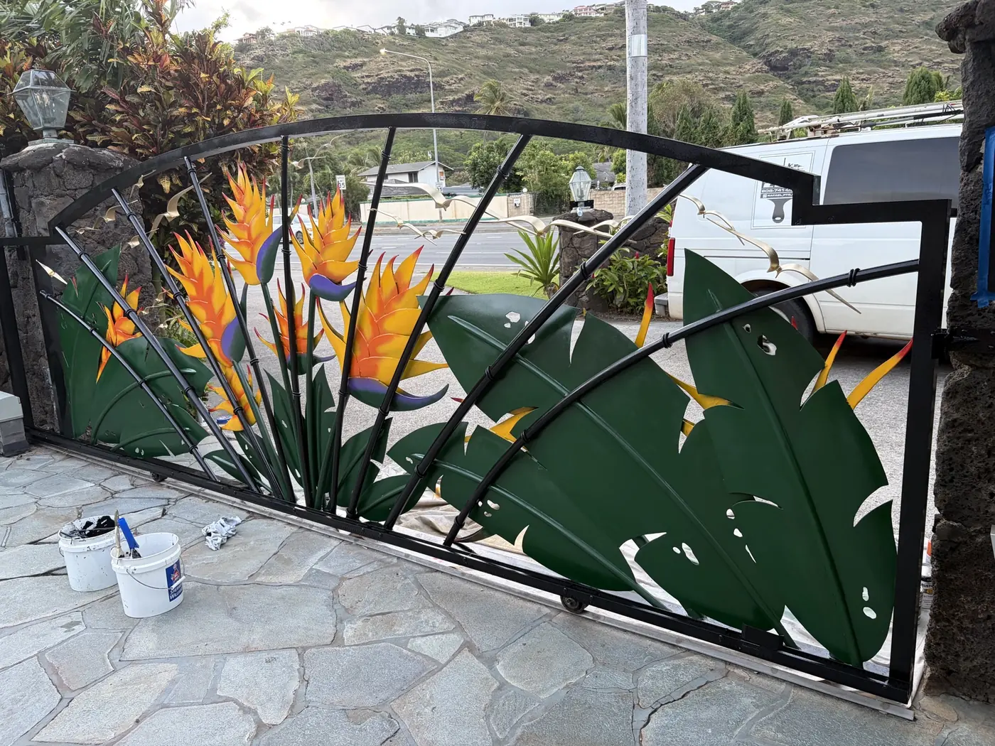 Gate detail looking out to the Hawaii Kai ridgeline, deep green sculpted leaves wrapping the bird-of-paradise centerpiece