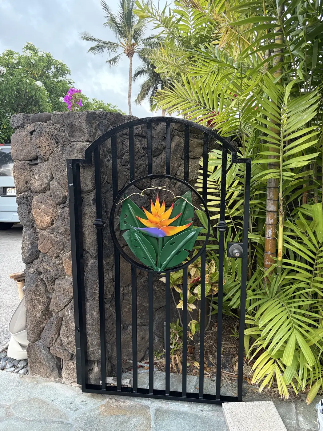 Matching side-gate medallion with a single hand-painted bird-of-paradise inset against the lava-rock pillar, palms framing the view