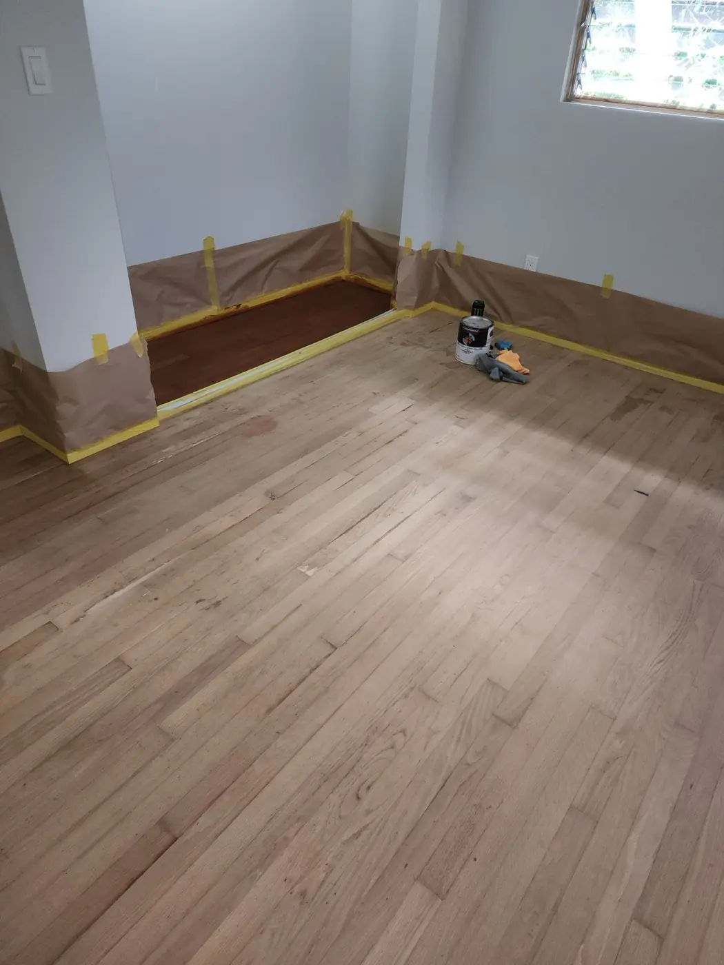 Hardwood floor prep: room cleared, masking in place along the wall line