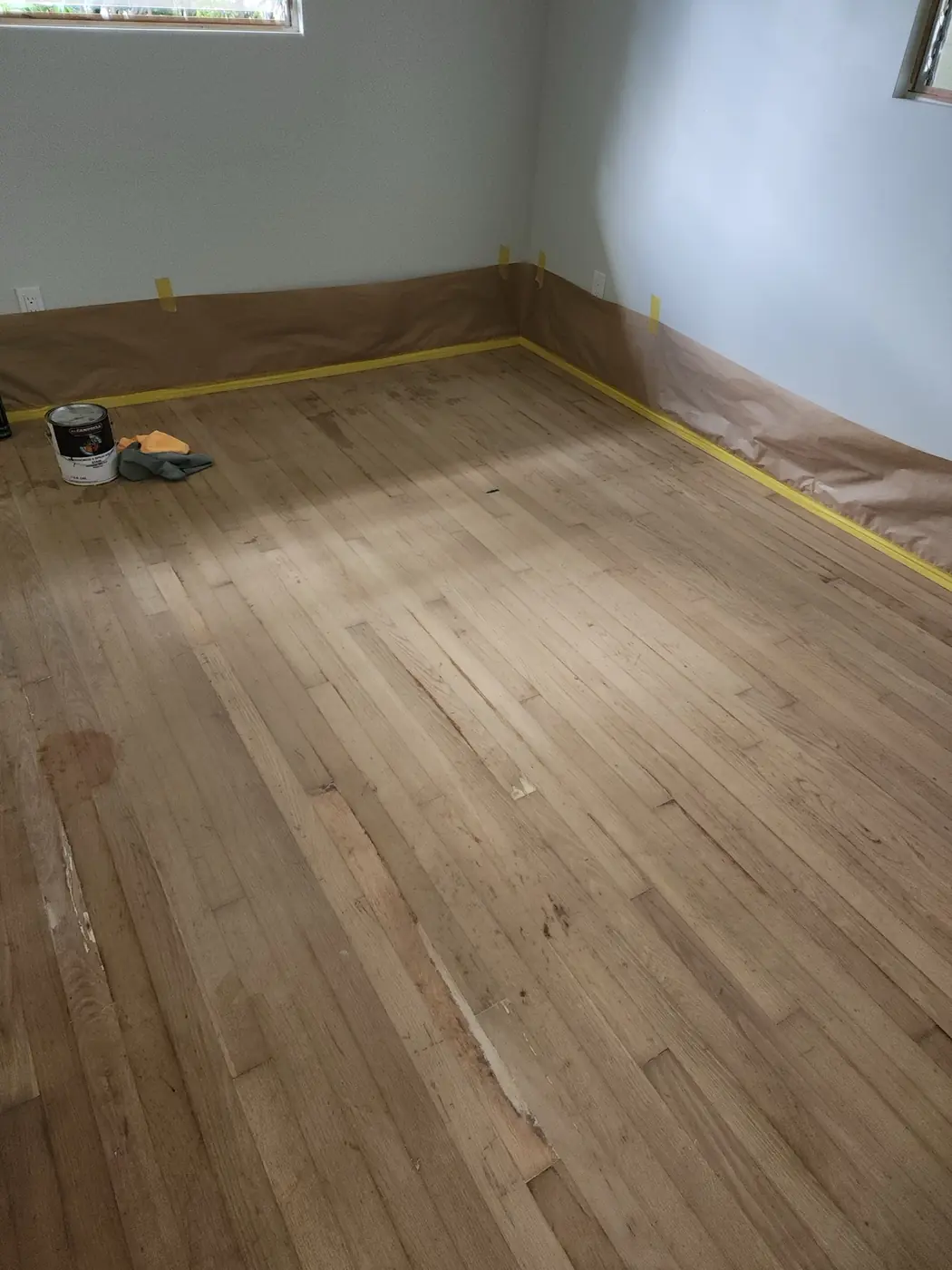 Hardwood floor prep: original plank sanded, baseboards masked, ready for stain
