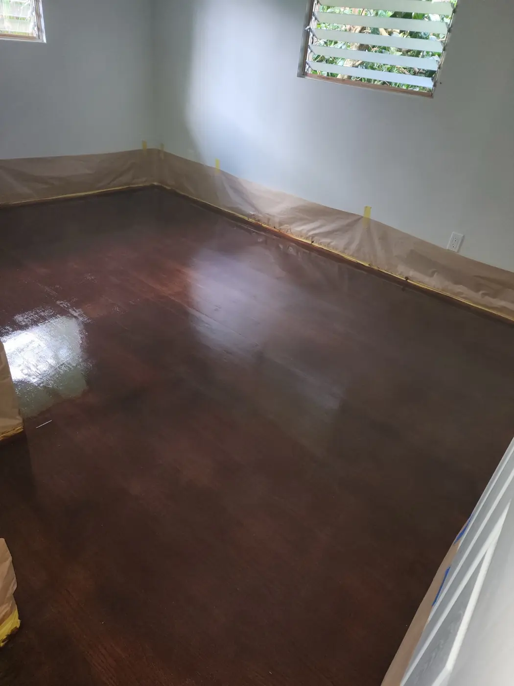 Restored hardwood plank floor finished in a warm walnut tone, prep paper still taped to the baseboards