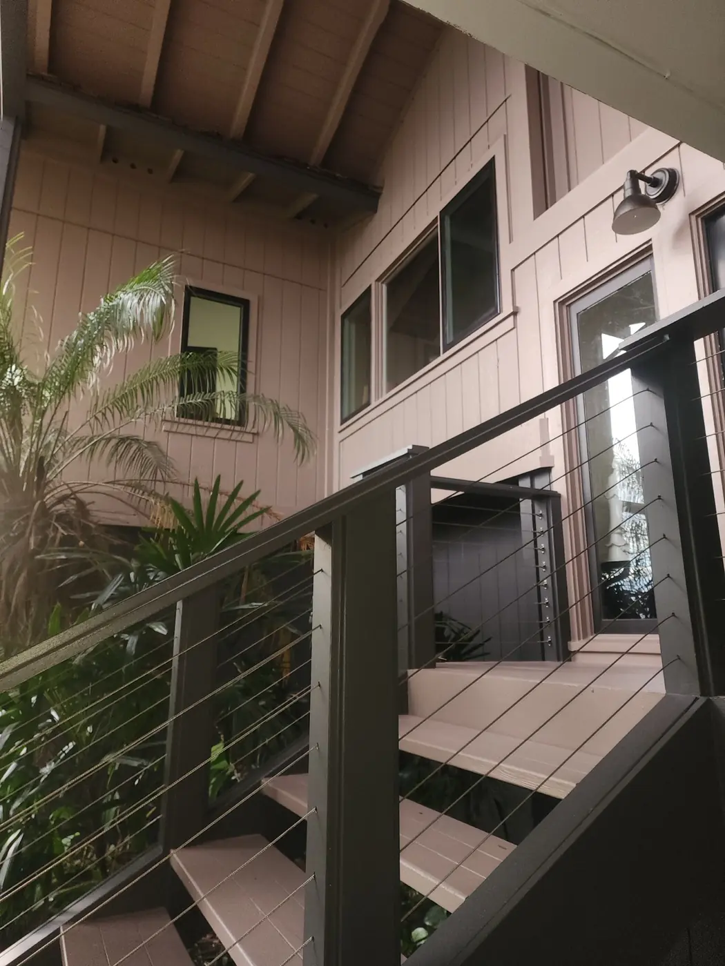 Hawaii Kai multi-story residence finished in soft peach with deep slate trim, cable-railing balconies and palms framing the entry