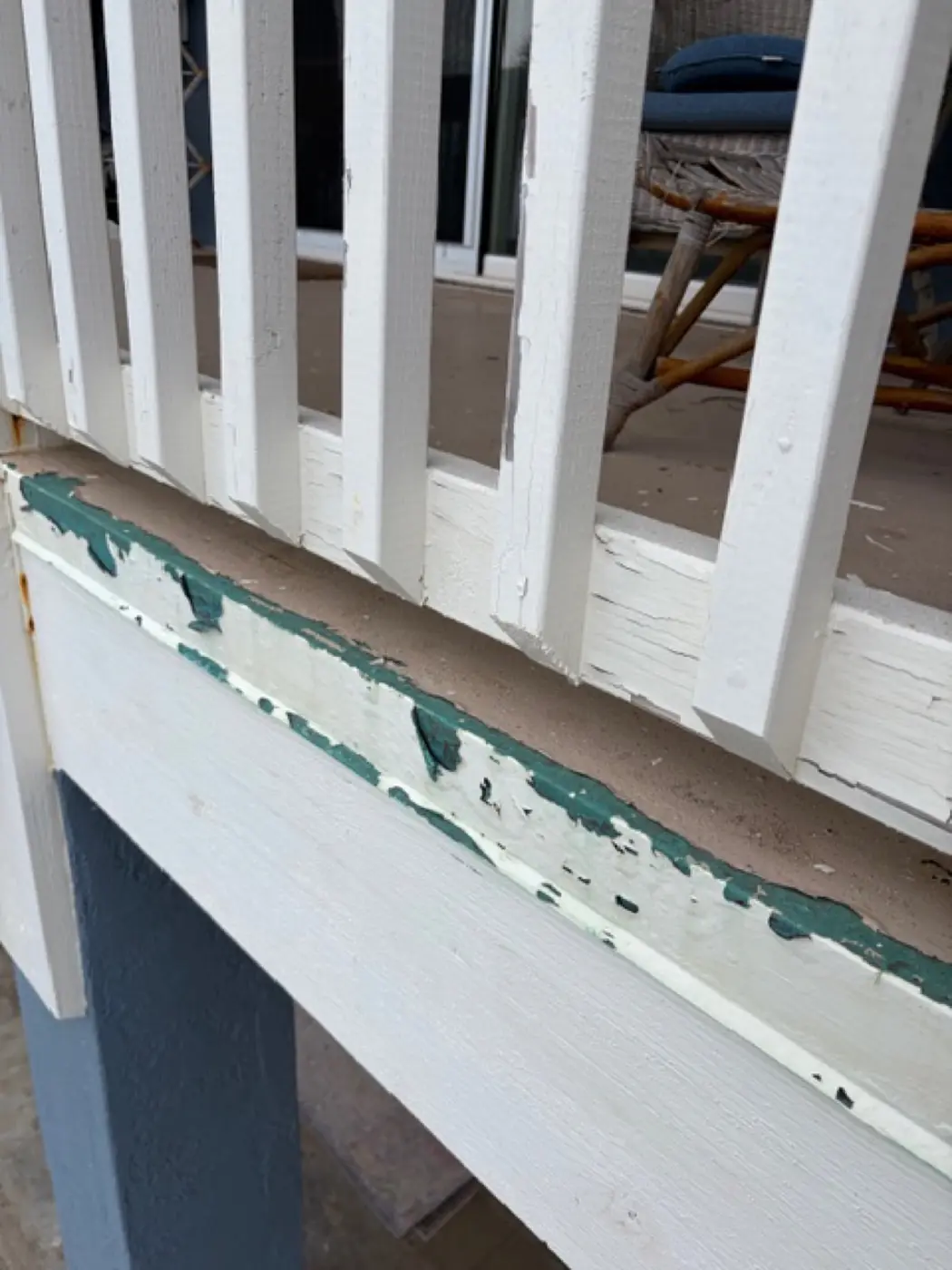Close-up of an oceanside railing with severe paint peeling, teal undercoat exposed where salt air has eaten through prior topcoats