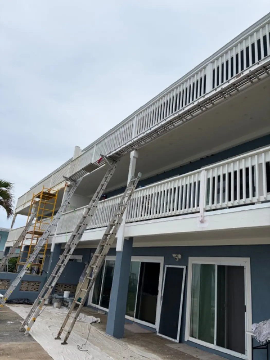 Salt-air spec project in progress: scaffolding and extension ladders set against the multi-story exterior, surface prep underway before the slate-blue topcoat