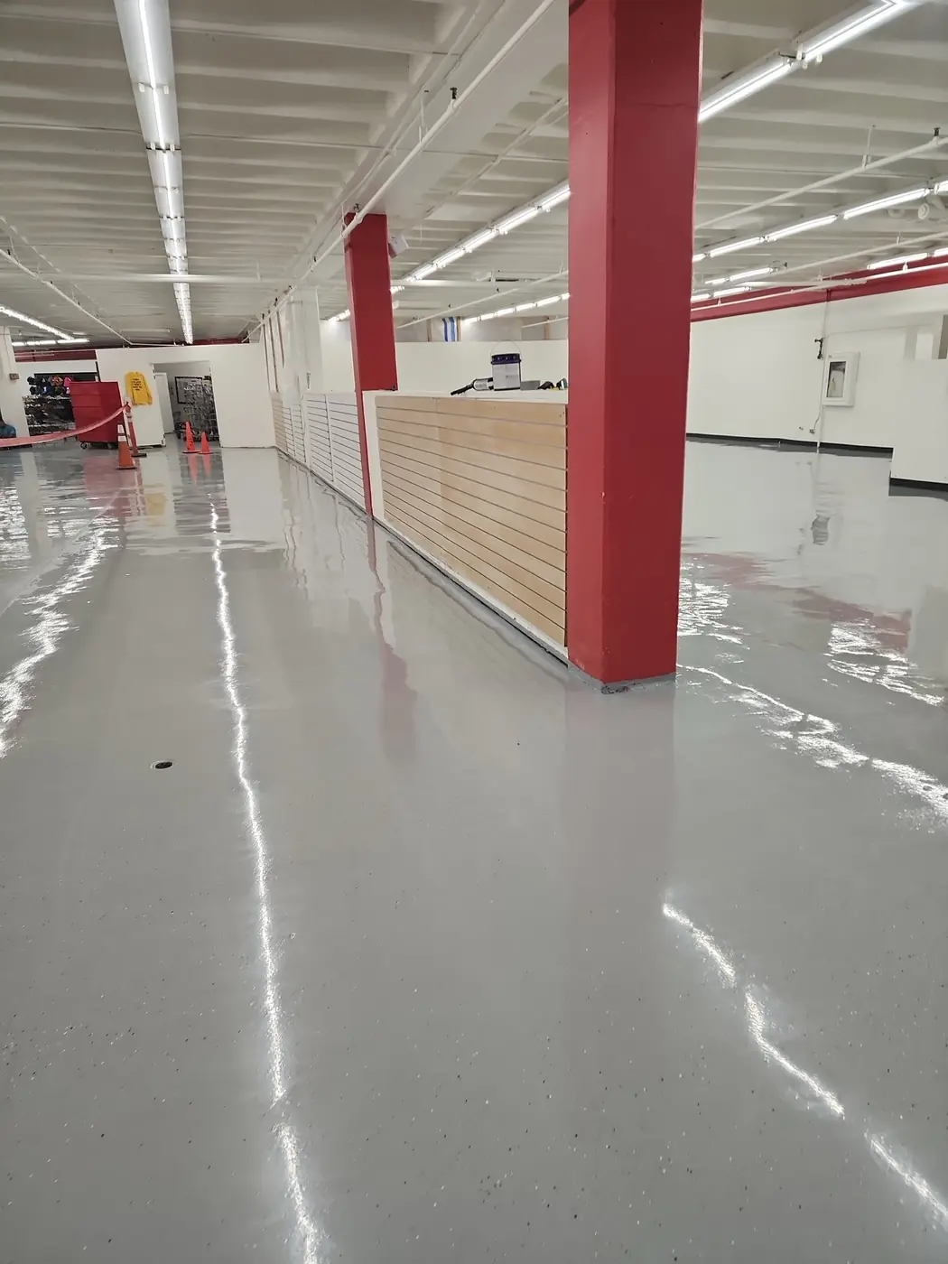 Salvation Army Kailua store interior: freshly poured gray epoxy floor reflecting overhead lights down a long aisle, red structural columns and a wood checkout counter visible at the back