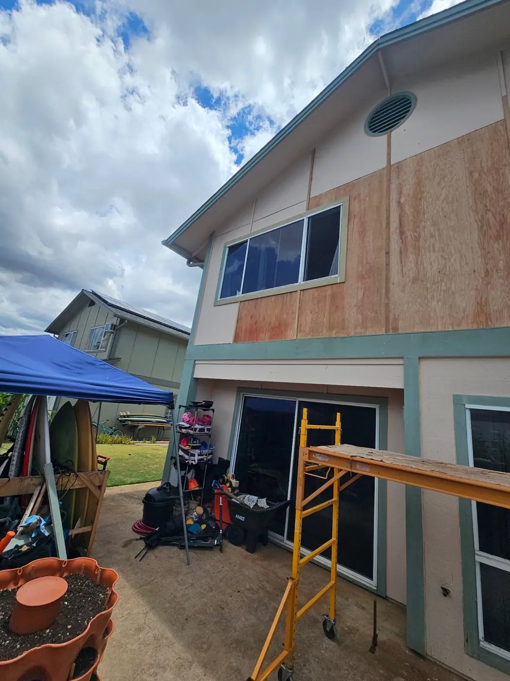Two-story exterior with a fresh plywood patch sistered into the second-floor wall after rot was cut out, scaffold in place
